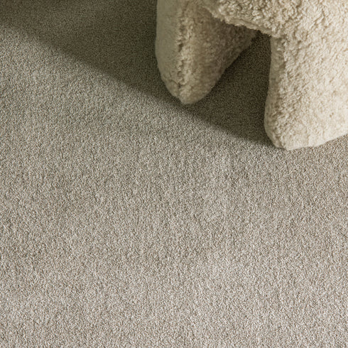 Balta Classic Charm carpet in Heathers (beige), featured in a stylish room with a woolly stool, minimalist décor, and soft natural lighting, creating a warm and inviting atmosphere.