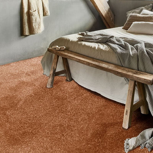 Luxurious GAIA® Dorado carpet in a rich sand hue with warm orange tones, adding depth and warmth to a stylish bedroom setting.