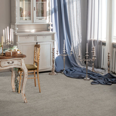 Elegant interior featuring Riviera Home Kensington carpet in a soft neutral tone. The premium handwoven wool flooring complements vintage furniture, ornate candleholders, and flowing drapery, creating a refined and timeless ambiance.