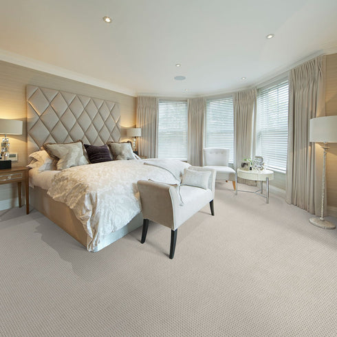 Luxurious bedroom featuring Riviera Home Lace wool carpet in a soft neutral tone, complementing an elegant tufted headboard, plush bedding, and sophisticated decor.