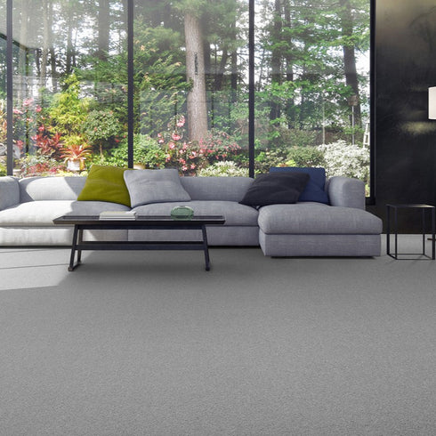 Lano Romance carpet in Silver 1 (a grey), beautifully laid in a modern living room, featuring a sleek sofa and full-length windows that offer a stunning view of nature, enhancing the serene and elegant ambiance.