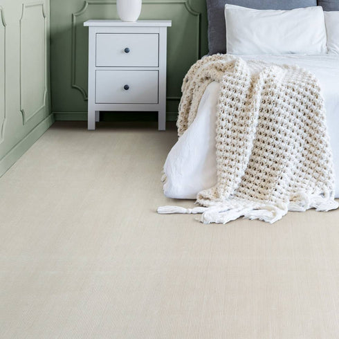 Elegant bedroom featuring Riviera St Tropez luxury carpet in a soft neutral tone, complemented by sage green panelled walls, a white bedside table with fresh flowers, and a cozy textured throw on the bed. A perfect blend of sophistication and comfort.