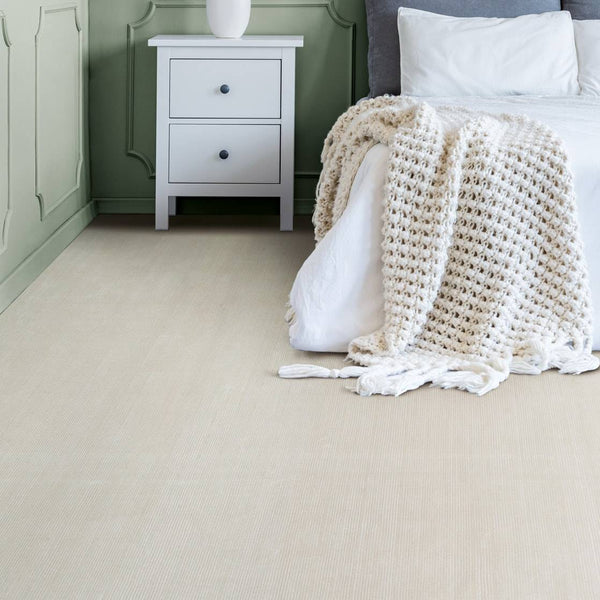 Elegant bedroom featuring Riviera St Tropez luxury carpet in a soft neutral tone, complemented by sage green panelled walls, a white bedside table with fresh flowers, and a cozy textured throw on the bed. A perfect blend of sophistication and comfort.