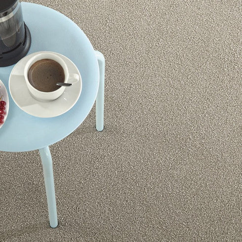 Lano Sweet Elegance carpet in Flax (beige), captured from a top-down view, showcasing its plush texture with a sleek table on top, featuring a black coffee cup, creating a cozy and refined setting.