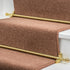Stairrods UK Eastern Promise Dune in brass, beautifully fitted on a brown beige carpet runner, enhancing the elegance of white wooden stairs with a classic gold finish.